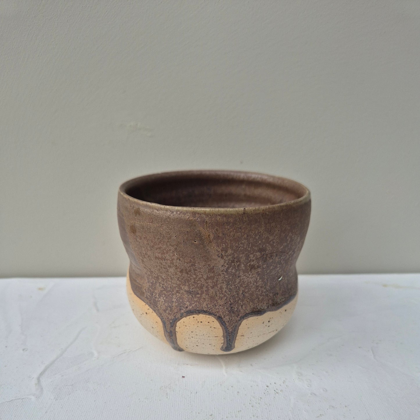 Ceramic cup with brown and beige glaze on a light gray background