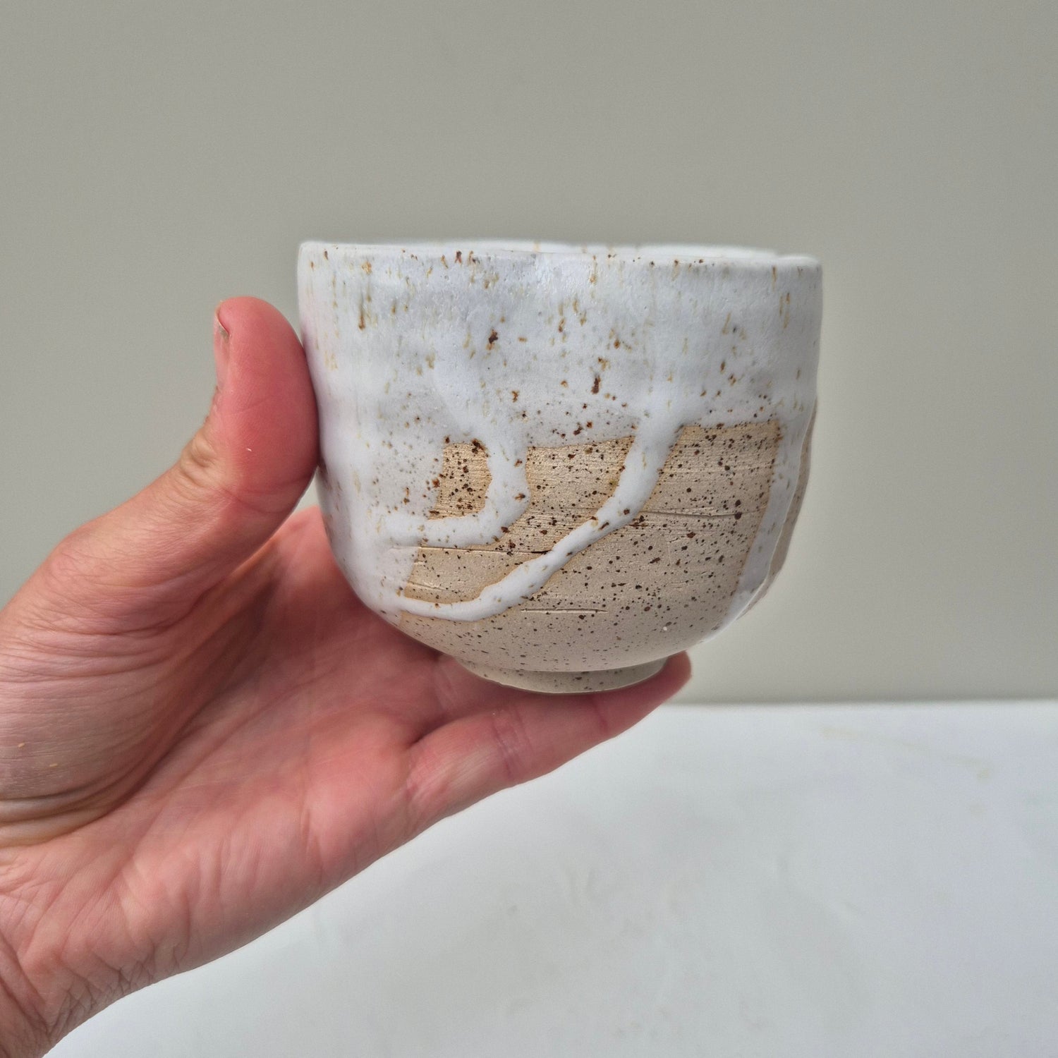 Hand holding a small ceramic bowl against a plain background
