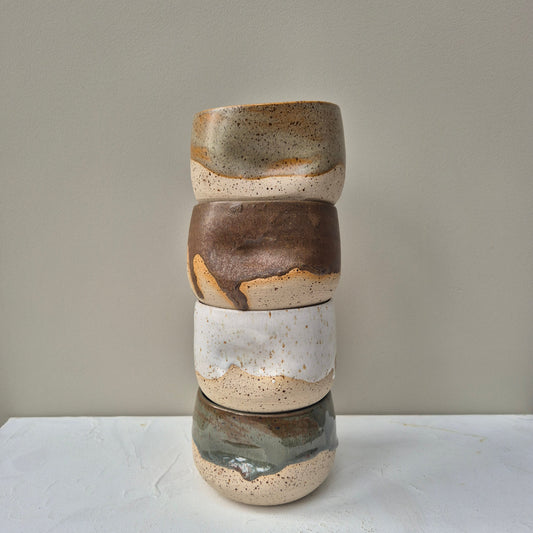 Stack of ceramic pots with layered colors on a neutral background