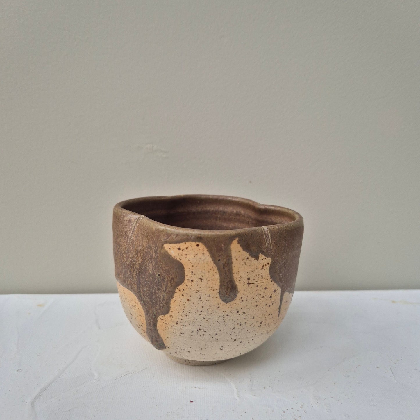 Small ceramic cup with brown and beige speckled design on a white background