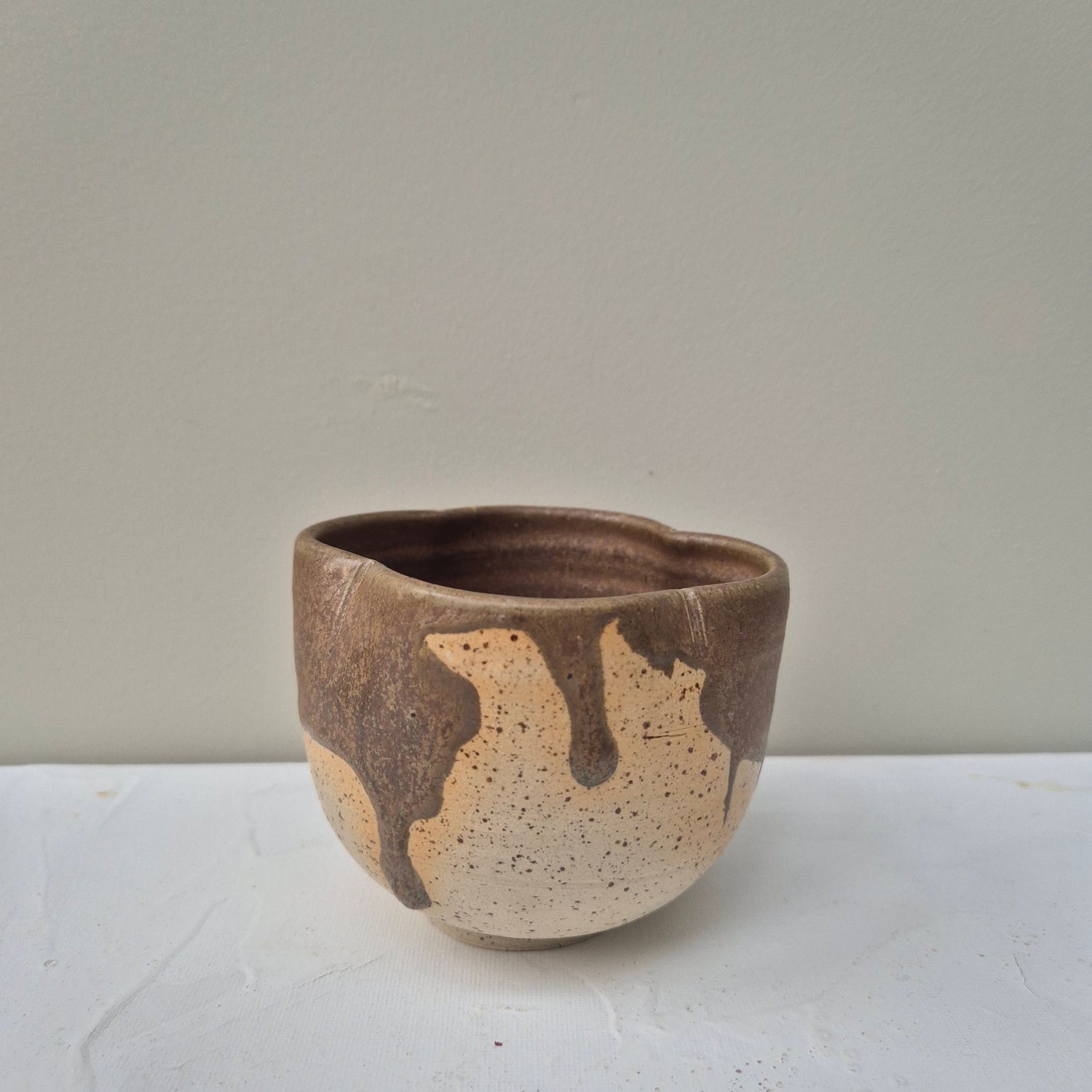Small ceramic cup with brown and beige speckled design on a white background